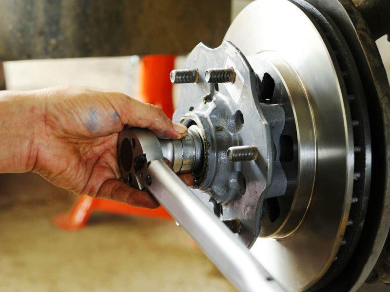 A persons hand using a torque wrench to tighten a bolt on a cars brake rotor assembly. The image shows detailed close-up of the mechanical components.