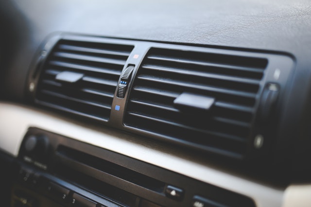 Close-up view of a cars dashboard air vents. The vents have horizontal slats with small adjustment levers, surrounded by a black panel. The dashboard also shows part of the cars audio or control system below the vents.