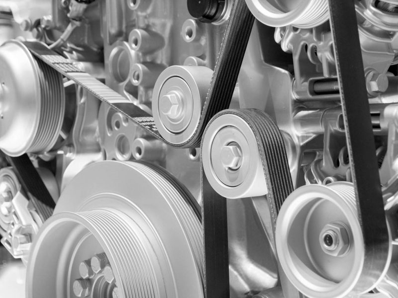 Close-up of a complex mechanical engine, featuring various pulleys and belts in an intricate configuration. The metallic components exhibit a shiny, silver appearance, highlighting the detailed engineering of the machinery.